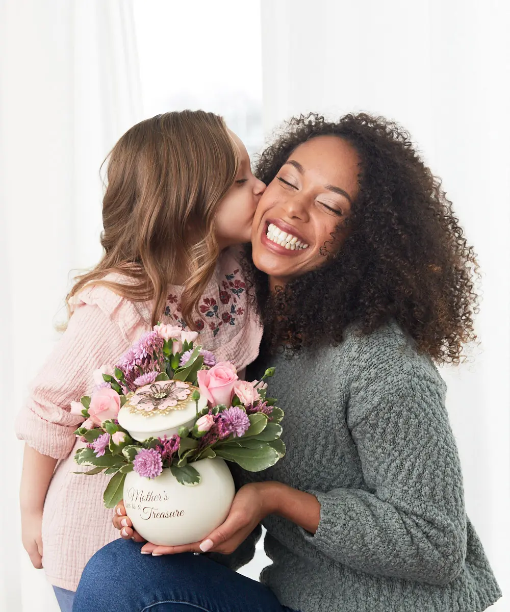 regalos para madres no tradicionales con hija pequeña besando a la madre con flores