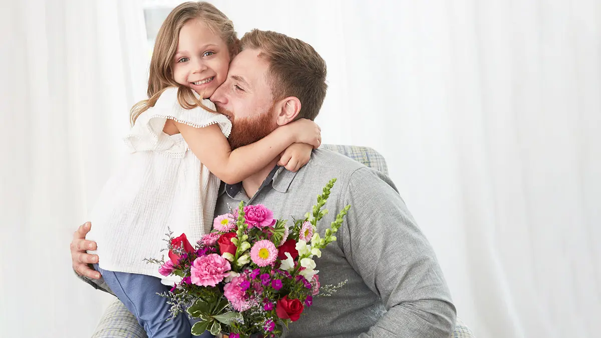 Historia del día de la madre con padre e hija abrazándose con flores.