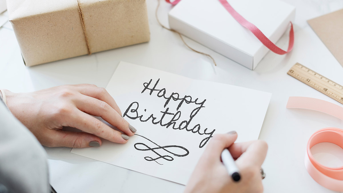 deseos de feliz cumpleaños con una mujer escribiendo una tarjeta de cumpleaños