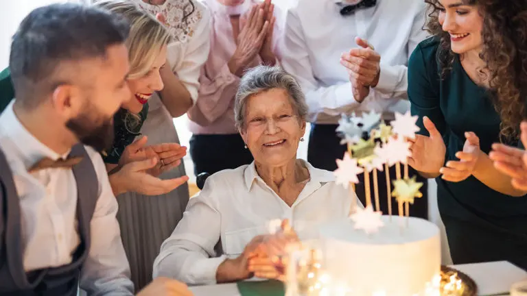 Ideas de fiesta de cumpleaños para personas mayores con familiares aplaudiendo alrededor de la mesa