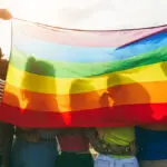 Young diverse people having fun holding lgbt rainbow flag outdoor Main focus on african guy back