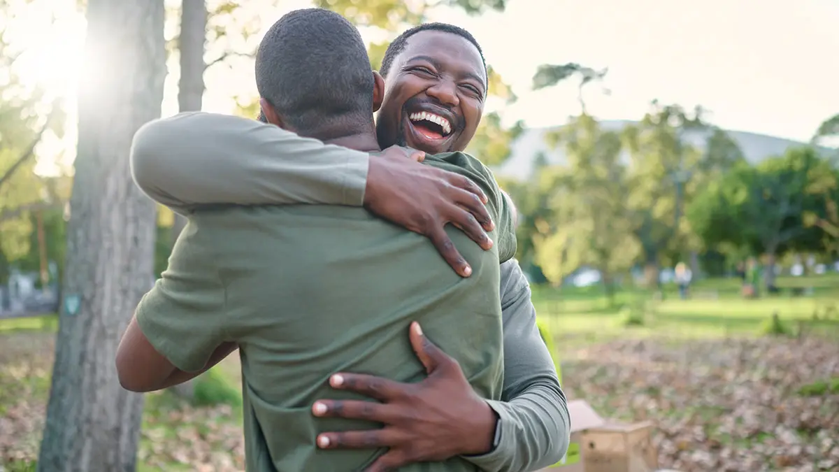 Charity, happy and hug with volunteer friends in a park for community, charity or donation of time together. Support, teamwork or sustainability with a black man and friend hugging outdoor in nature