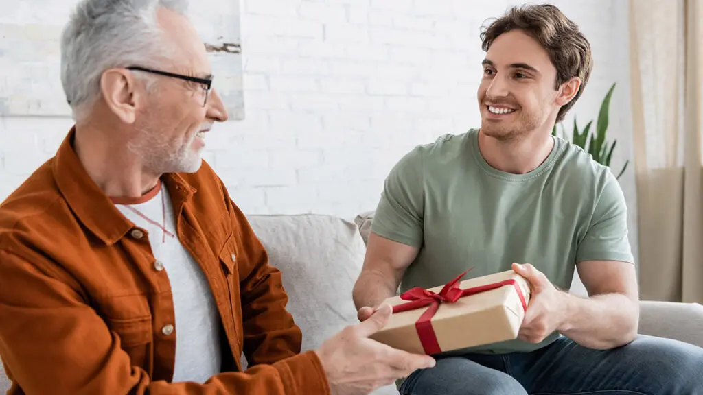 happy man congratulating dad on fathers day and giving him gift