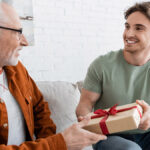 happy man congratulating dad on fathers day and giving him gift