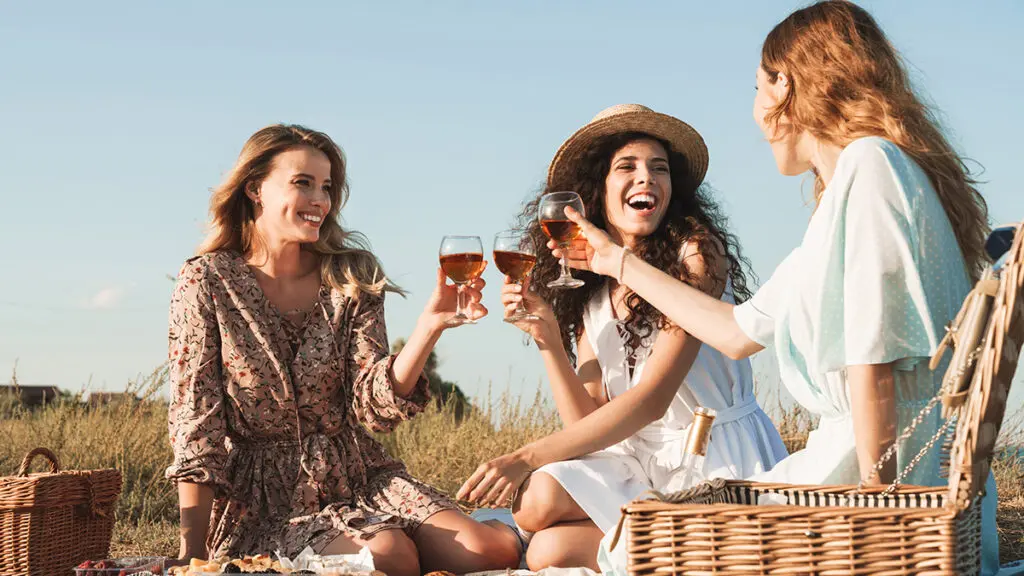 Foto de tres jóvenes felices bebiendo vino tinto mientras beben