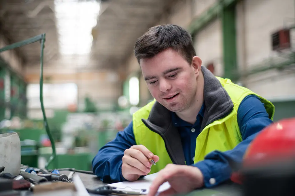 Young man with Down syndrome working in industrial factory, social integration concept.