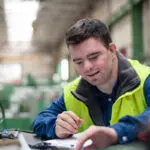 Young man with Down syndrome working in industrial factory, social integration concept.