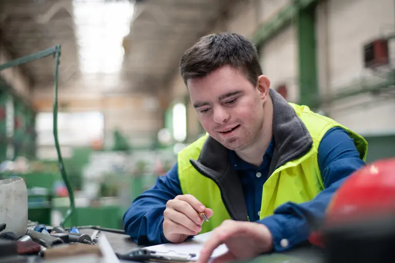 Young man with Down syndrome working in industrial factory, social integration concept.