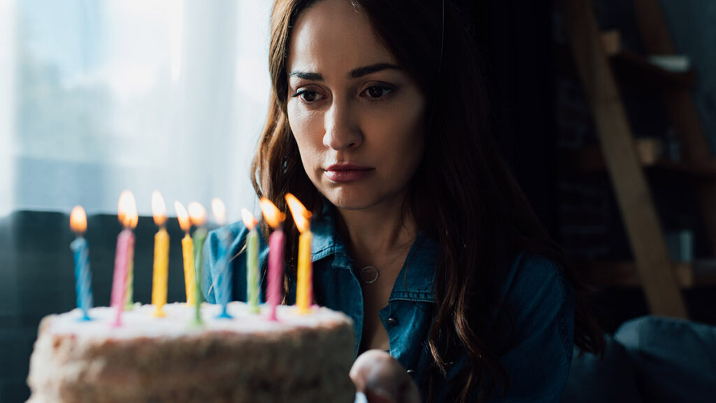 selective focus of sad woman looking at birthday cake with candl