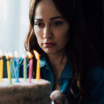 selective focus of sad woman looking at birthday cake with candl