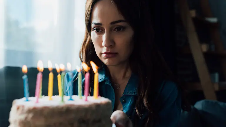 selective focus of sad woman looking at birthday cake with candl