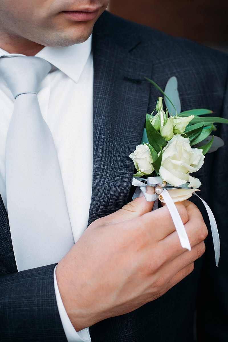 A stylish groom in a blue suit, tie and white shirt touches a bo
